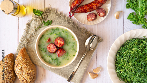Table with Portuguese-style soup called Caldo Verde and bread, Cabbage julienne, oil, and chorizo sausage. Flat lay