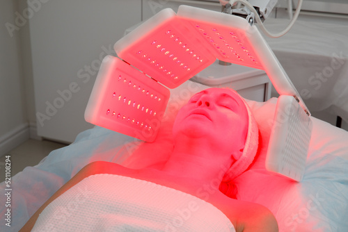 An elderly woman undergoes a facial rejuvenation procedure. Woman face lt Red light treatment At beauty clinic. Cosmetology.