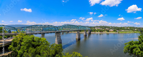 a panoramic shot of the rippling waters of the Tennessee River with the Walnut Street Bridge over the water surrounded by lush green trees with blue sky and clouds in Chattanooga Tennessee USA