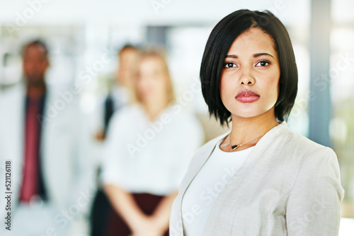 Serious, focused and confident female lawyer looking at the camera and standing in her office with her team. Portrait of a leader, smart and intelligent attorney that is tough and resilient