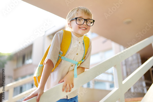 Smart little child with backpack on the stairs of school building. Quality education for children. Portrait of funny nerd schoolboy with big glasses. Vision problems. Back to school concept.