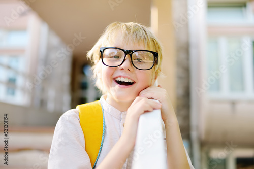 Smart little child with backpack on the stairs of school building. Quality education for children. Portrait of funny nerd schoolboy with big glasses. Vision problems. Back to school concept.
