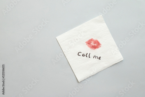 Paper napkin with lipstick mark and words CALL ME on grey background, top view. Space for text