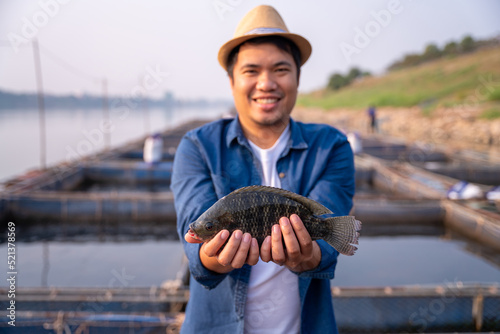 Aquaculture farmer hold quality tilapia yields in hand, guaranteeing integrity in organic bio-aquaculture. Fish is a high-quality protein food source. Commercial aquaculture in the Mekong River.