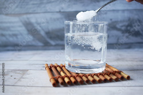 pouring white sugar in a glass of water on table 