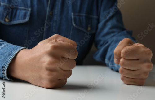 Man clenching fists at table while restraining anger, closeup