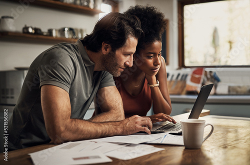 Couple with a laptop doing finance paper work, paying debt insurance loans or online ebanking together at home. Two serious people planning and looking at financial document, bills rate for mortgage