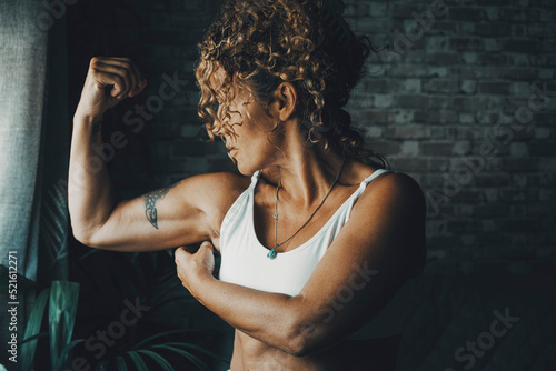 One middle age 50s woman at home doing biceps muscle. Concept of energy and power lady doing sport activity and fitness workout. Healthy body positive lifestyle. Female people empowerment portrait