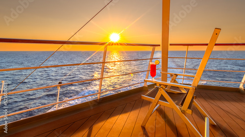 Vue d'une chaise longue avec un cocktail sur le pont d'un navire de croisière au coucher de soleil dans le sillage du navire de croisière. Vue depuis la poupe du navire. 