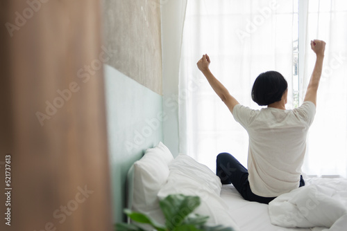 Rear view, Young Asian man sitting stretching on the bed during early morning, Waking up
