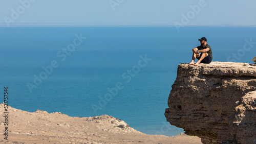A man looking out across the landscape fropm a cliff edge. Deep in thought, with the sea and rocks below him.