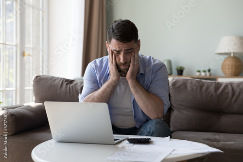 Millennial man counted income and expenses looks upset because of lack of funds for monthly mortgage payments feels desperate sit near heap of bills feels stressed. Financial failure, debts concept