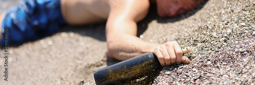 A drunk man with a bottle lies on the wet sand, blurry