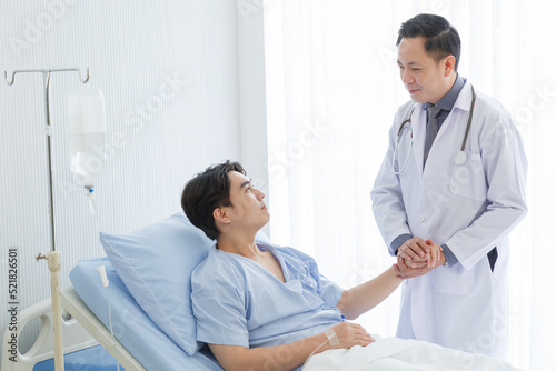 Senior doctor and young male patient who lie on the bed while checking pulse, consult and explain with nurse taking note and supporting in hospital wards.