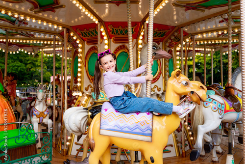 a child girl in an amusement park rides on a carousel and smiles with happiness, the concept of weekends and school holidays