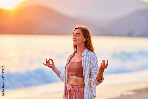 Portrait of calm serene peaceful woman with closed eyes in lotus position meditates and enjoys beautiful moment life on the seashore at sunset time