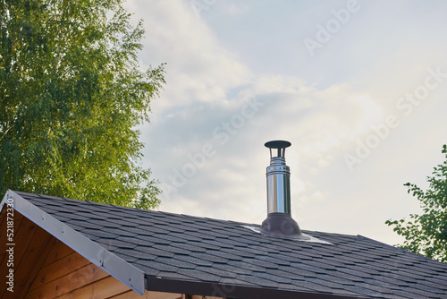 Stainless steel metal chimney pipe on the roof of the house against the sky.