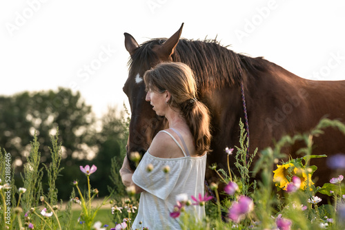 Frau schmust mit Pferd im Blumenfeld