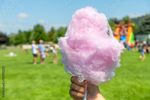 A hand holding pink cotton candy at an outdoor summer fair with festival goers blurred behind.