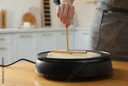 Woman cooking delicious crepe on electrical pancake maker in kitchen, closeup