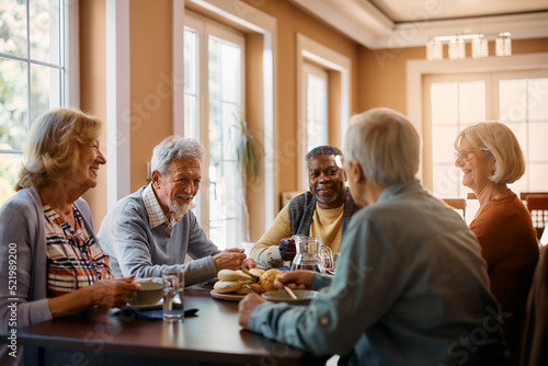 Happy seniors talk while eating lunch at residential care home.