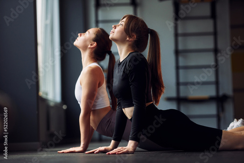 Doing stretches. Two women in sportive clothes have fitness day in the gym together