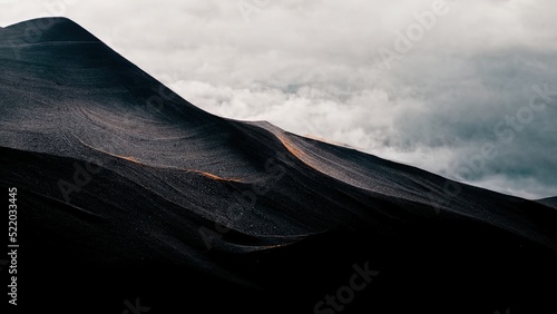 Minimal dark wallpaper. Black mountain with grey clouds, sand dunes, sombre, moody 4k background.