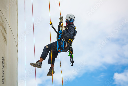 Male worker inspection wearing safety first harness rope safety line working at a high place on tank roof spherical gas blue sky