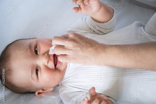 Mom wipes the baby's drool with a napkin. Baby care, teething, drooling.
