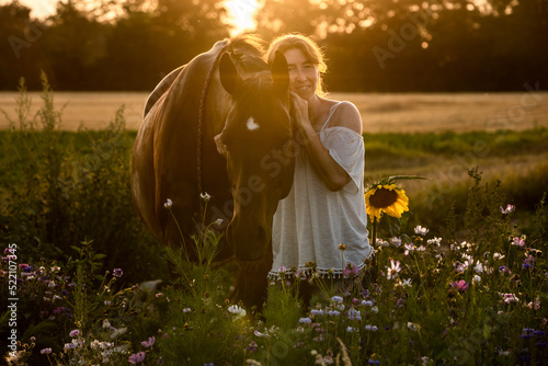 Frau mit Pferd bei Sonnenuntergang im Blumenfeld
