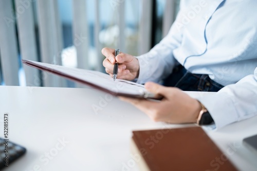 Portrait of  Asian Business woman working from office taking reading and writing notes in note pad working on laptop computer  in her workstation