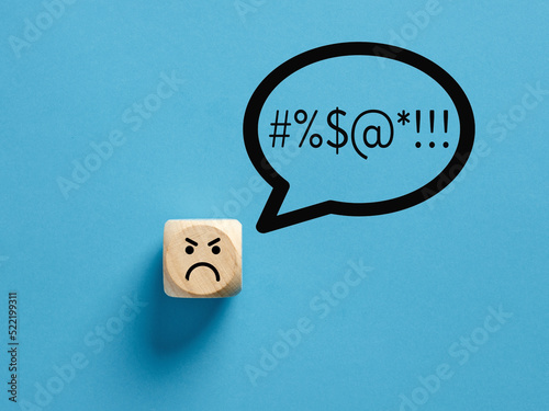 Angry face icon on a wooden cube with swearing or swearwords icons in a speech bubble.