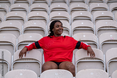 Smiling athletic woman sitting on chair at empty stadium