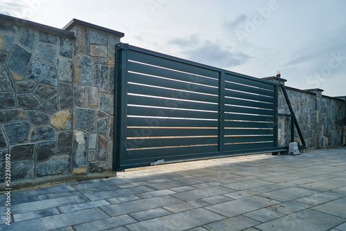 Wide automatic sliding gate with remote control installed in high stone fense wall. Security and protection concept