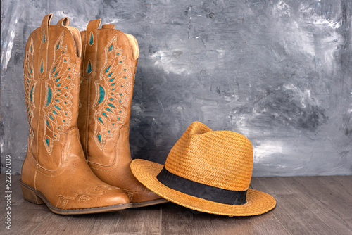 Leather cowgirl boots with a pattern and a hat stand on the floor against a gray wall.