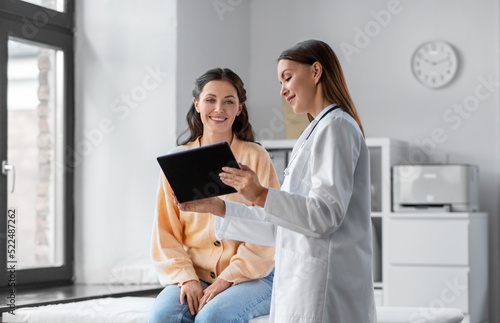 medicine, healthcare and people concept - female doctor with tablet pc computer talking to smiling woman patient at hospital