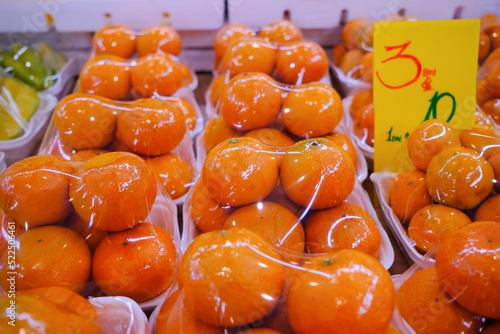 Fresh oranges at market stall display wrapped with plastic film wrap for protection of the fruits. The plastic wrappers are wasteful and unsustainable for the environment.