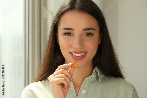 Young woman taking dietary supplement pill indoors
