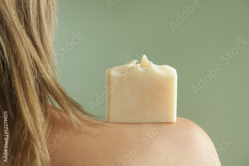 Young Caucasian woman holding soap bar on her shoulder. Natural handmade organic skin care cosmetic.