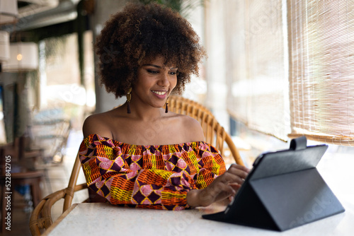 Beautiful young African girl smiling with tablet inside restaurant.