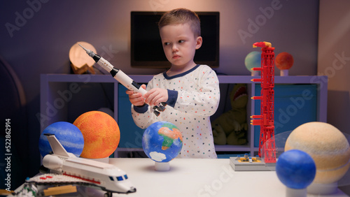 Little blonde boy kid plays with spaceship from constructor, flies near planets of solar system in evening. Child imagines himself as pilot of spaceship. Desire fly in space, flying on spaceship.