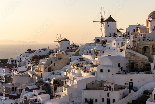  Whitewashed houses and windmills in Oia in warm rays of sunset on Santorini island. Greece