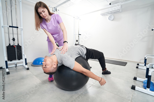 Female doctor helping man to perform physical therapy exercise