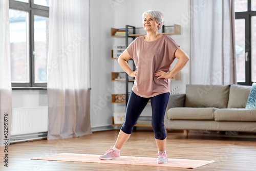 sport, fitness and healthy lifestyle concept - smiling senior woman exercising on mat at home