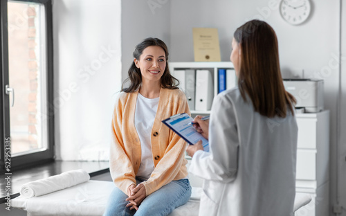 medicine, healthcare and people concept - female doctor with clipboard talking to smiling woman patient at hospital