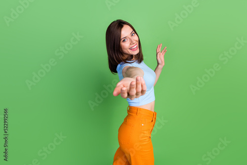 Profile portrait of adorable positive girl raise arm palm invite you isolated on green color background