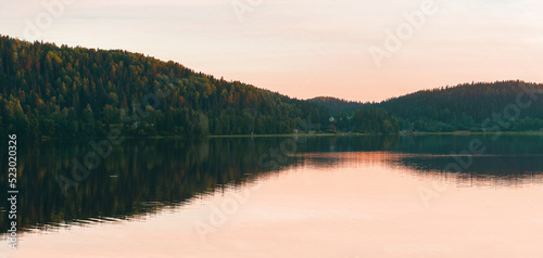 Panoramic view of forest lake in the evening fog reflecting in water. Summer travel vibes. Orange pink sundown. Natural background. An ideal backdrop for ecological design projects