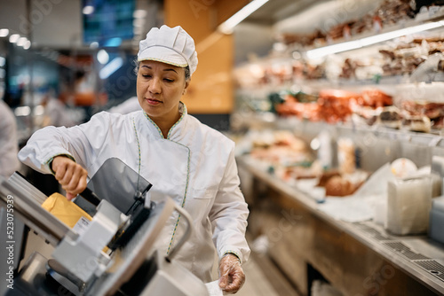 Supermarket worker using slicer at delicatessen section.