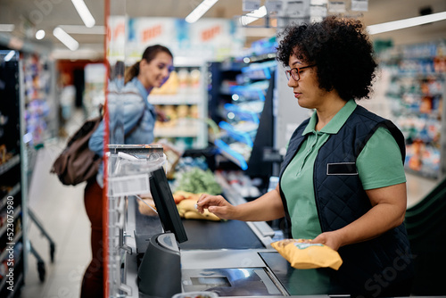 Female cashier scanning products at supermarket checkout.