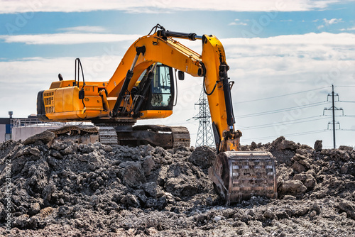 A powerful caterpillar excavator digs the ground against the blue sky. Earthworks with heavy equipment at the construction site.
